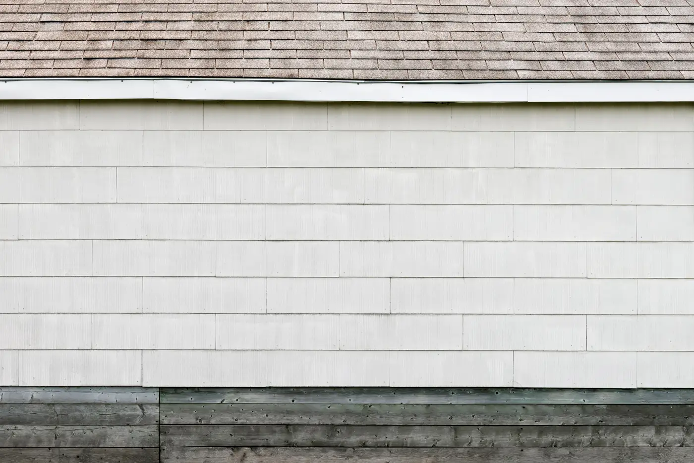 Close-up of an asphalt composition shingle roof edge above wood siding.