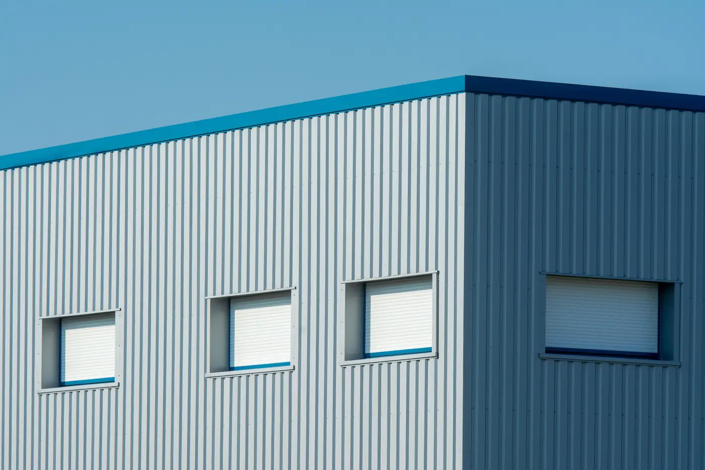 The corner of a corrugated metal commercial building meeting at a sharp edge against a blue sky.