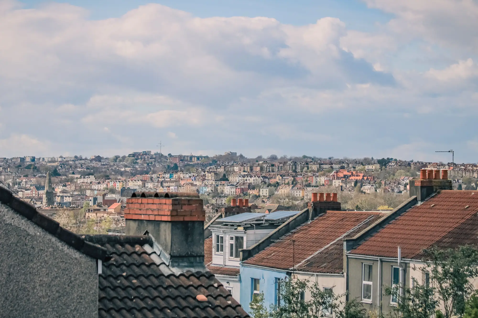 Pitched roofs and chimneys in the foreground, a hillside of terraced houses beyond