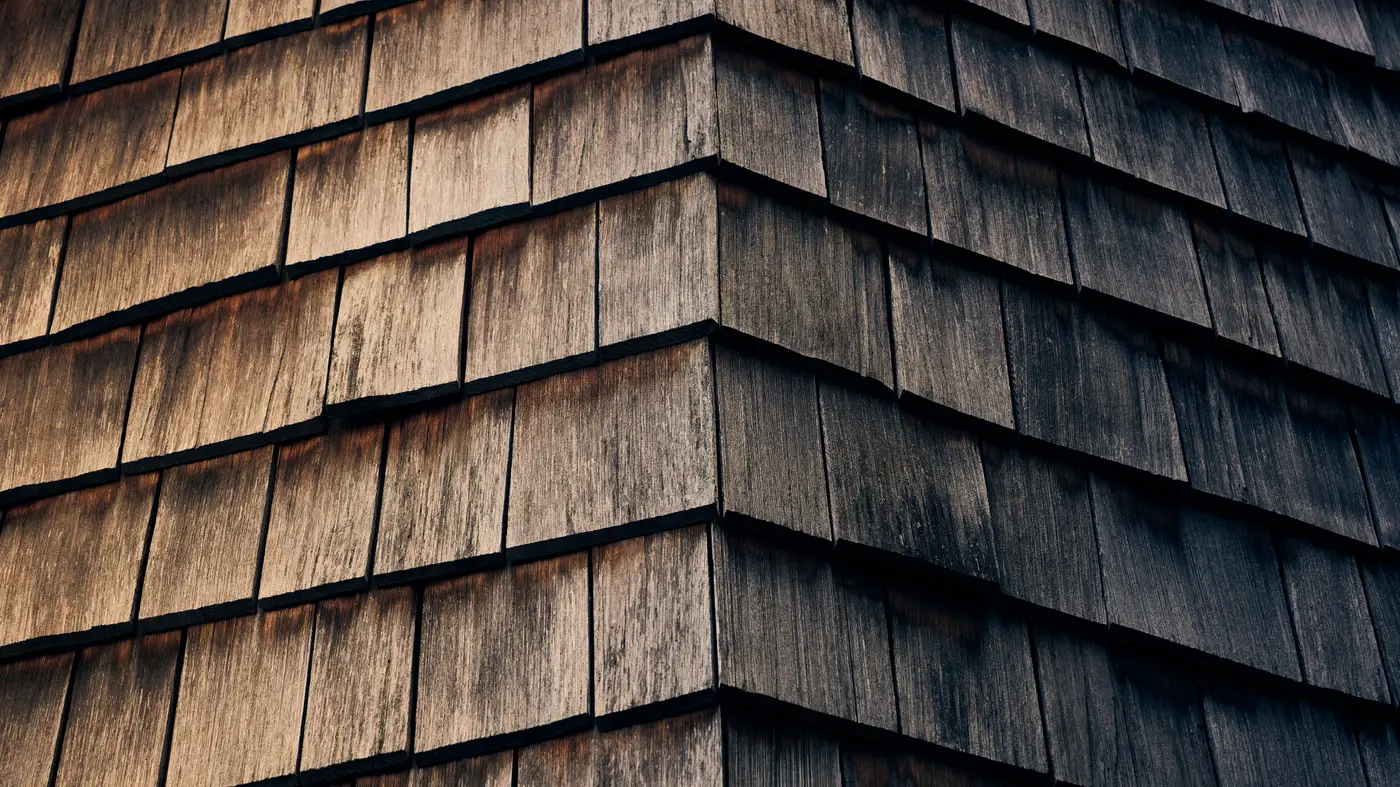 Close-up of a weathered wood shake shingle roof at a hip corner.